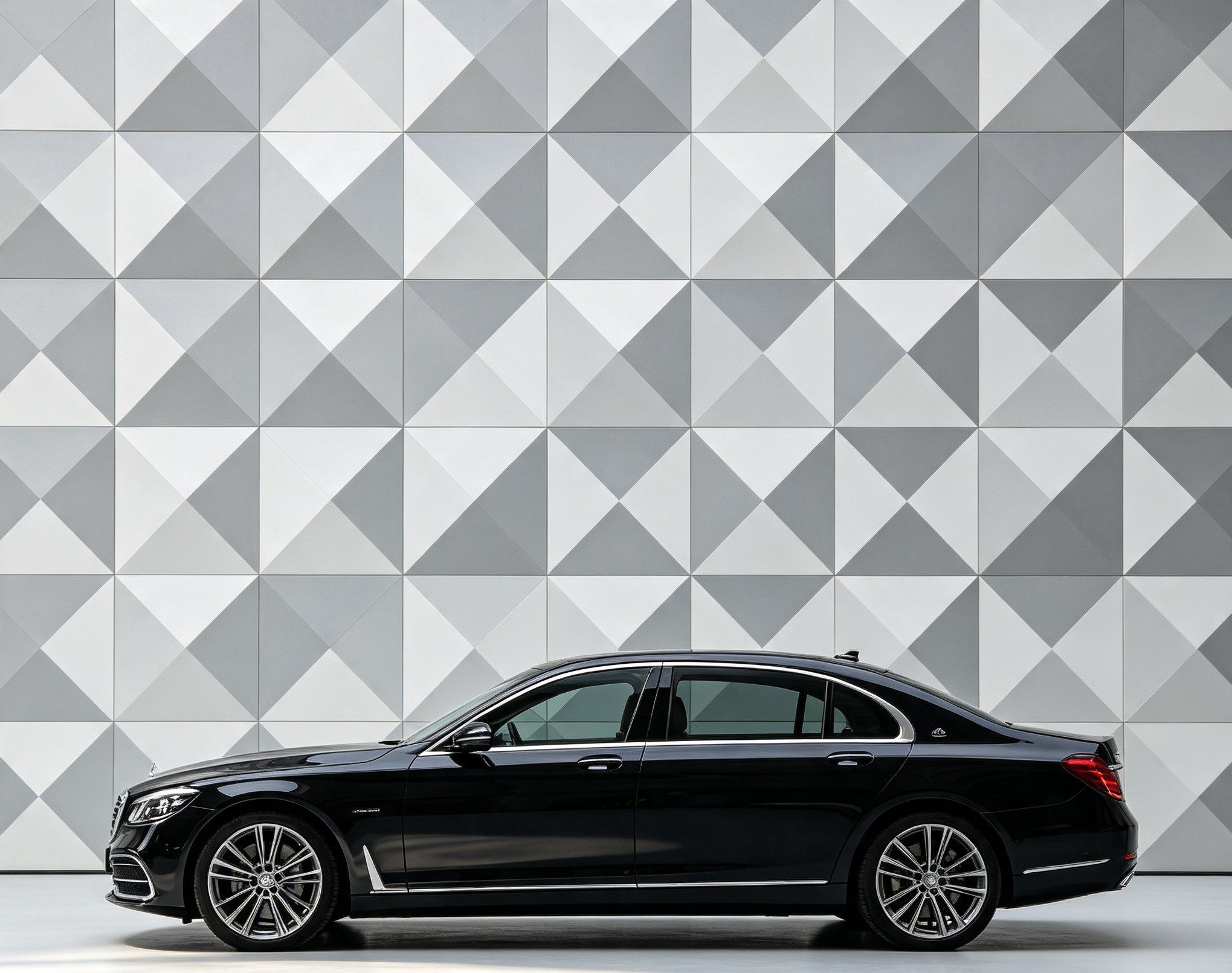 Berline de luxe noire vue de profil devant un mur au motif géométrique gris et blanc